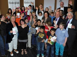 Die Kinder des Stadtteiltreffs Mainz-Gonsenheim mit Kinderliedermacher Oliver Mager (hinten rechts) sowie Familienministerin Irene Alt (vorne, 2. von links) sowie (von rechts) dem Lotto-Aufsichtsratsvorsitzenden Dr. Salvatore Barbaro, seinem Stellvertreter Walter Desch, dem Stiftungsvorsitzenden Magnus Schneider und Ministerpräsidentin Malu Dreyer.