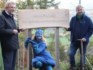 Heiner Rupsch (r.), 1. Vorsitzender Trinkwasserwald e.V., überreicht ein Spendenschild, das fortan an der Fläche in Nettelstedt stehen wird, an Initiator Paul Gauselmann (l.) mit Frau Wasser (m.) und Herrn Wald (nicht auf Bild), Symbolfiguren der Trinkwasserwald e.V. (Symbolbild)