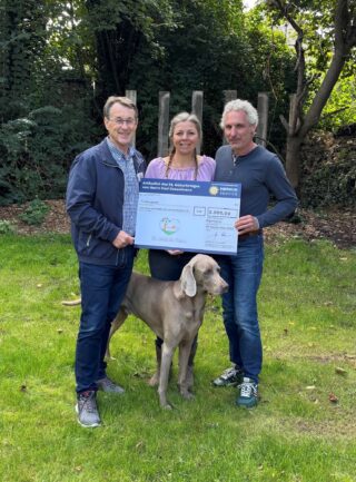 Joachim Mohrmann (links) überreicht Frank und Nicole Pape den Spendenscheck über 5.000 Euro. Auch Hund „Badman“ ist mit dabei. (Foto: Merkur Group)