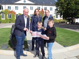 Fabian (9) und Theo (7) freuen sich mit ihren Eltern Natalia Wüllner-Fröhlich und Michael Fröhlich über die Schatzsuche. Die Hilfe von Espelkamps Bürgermeister Dr. Henning Vieker wird bei der Lösung gerne in Anspruch genommen. (Foto: Merkur Group)