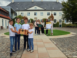 Neben Pauli (von links), Ben Luca, Julius und Linus, die die Schatztruhe für den „Tag des offenen Denkmals“ präsentieren, freuen sich auch Kirsten Beste, Larissa Mattlage, Angelina Horn, Nicole Kolwes und Sylvia Blaha auf die Aktionen am Schloss. Foto: Schloss Benkhausen