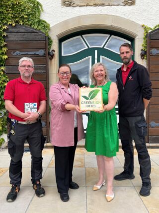 Prüferin Annett Reimers (Zweite von rechts) überreicht das „GreenSign“-Zertifikat Christian Schröder (Nachhaltigkeitsbeauftragter Schloss Benkhausen, von links), Larissa Mattlage (Direktorin Schloss Benkhausen) und Björn Hülshorst (Teamleitung Hausmeister). (Foto: Merkur Group)