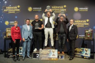 Kristina Kratz (Projektmanagerin), Thomas Nowarra (Direktor Merkur Spielbank Hohensyburg) und David Schnabel (Vorstand Merkur Casinos) (v.l.n.r.) gemeinsam mit den Gewinnern des Automatenturniers 2025 (auf dem Treppchen) bei der Siegerehrung. (Foto: Merkur Group)
