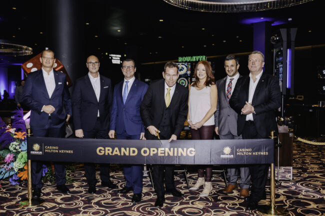 Lars Felderhoff (v.l.n.r.), Vorstandssprecher der Merkur Group, David Schnabel, Vorstand Merkur Casinos der Merkur.com AG, Mark Schertle, Chief Operating Officer bei Merkur Casino UK, Dave Scott, Spielbankdirektor Merkur Casino Milton Keynes, Jill Farnsworth, CEO von MyMiltonKeynes, Egemen Coskun, CFO von Merkur Casino UK und Sascha Blodau, General Manager UK der Merkur Group, während der feierlichen Durchtrennung des Bands. (Foto: Merkur Group)
